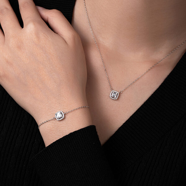 buste avce main sur l'épaule habillée d'une gourmette fine et un collier avec pendentif carré et serti de pierres synthétiques